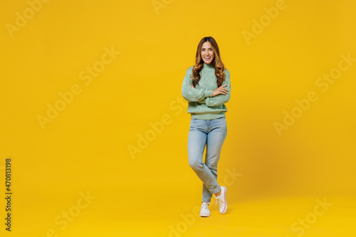 Full body young smiling confident fun woman 30s wearing green knitted sweater look camera hold hands crossed folded isolated on plain yellow color background studio portrait. People lifestyle concept.