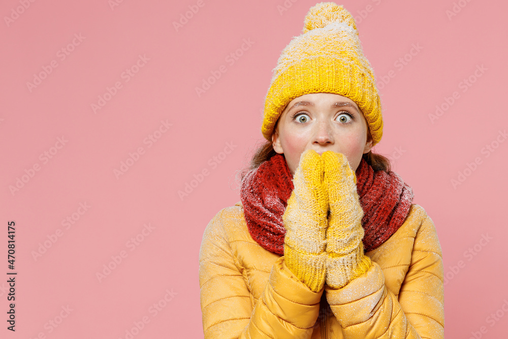 Surprised impressed astonished stupefied young woman 20s years old wears yellow jacket hat mittens looking camera cover mouth with hands isolated on plain pastel light pink background studio portrait. Surprised impressed astonished stupefied young woman 20s years old wears yellow jacket hat mittens looking camera cover mouth with hands isolated on plain pastel light pink background studio portrait.