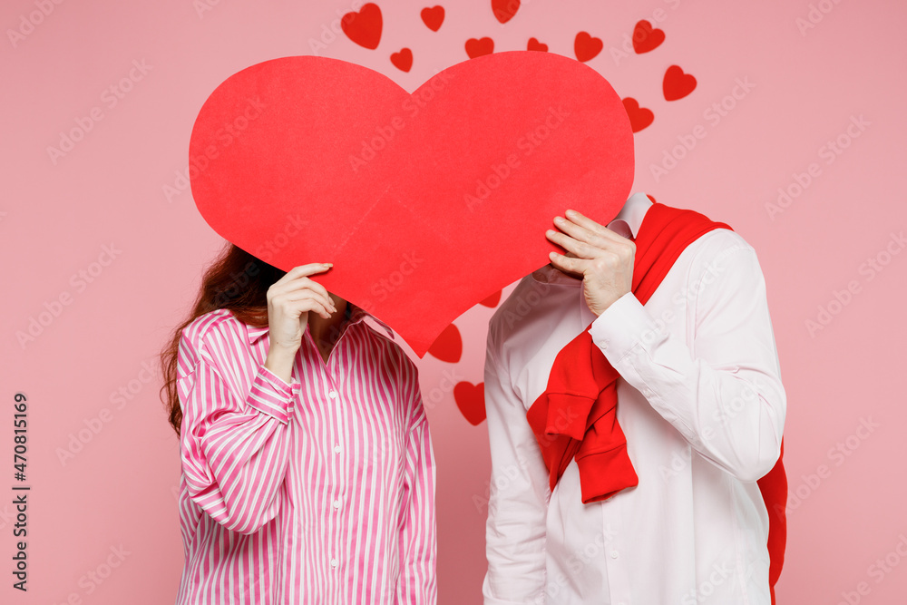 Young couple two friend woman man wearing casual shirt look camera hold big red heart kissing isolated on plain pastel pink background studio portrait. Valentine's Day birthday holiday party concept. Young couple two friend woman man wearing casual shirt look camera hold big red heart kissing isolated on plain pastel pink background studio portrait. Valentine's Day birthday holiday party concept.