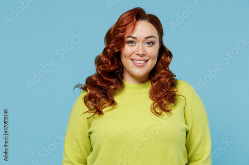 Obraz na plátně Young smiling satisfied happy chubby overweight plus size big fat fit caucasian woman wear green sweater look camera isolated on plain blue color background studio portrait
