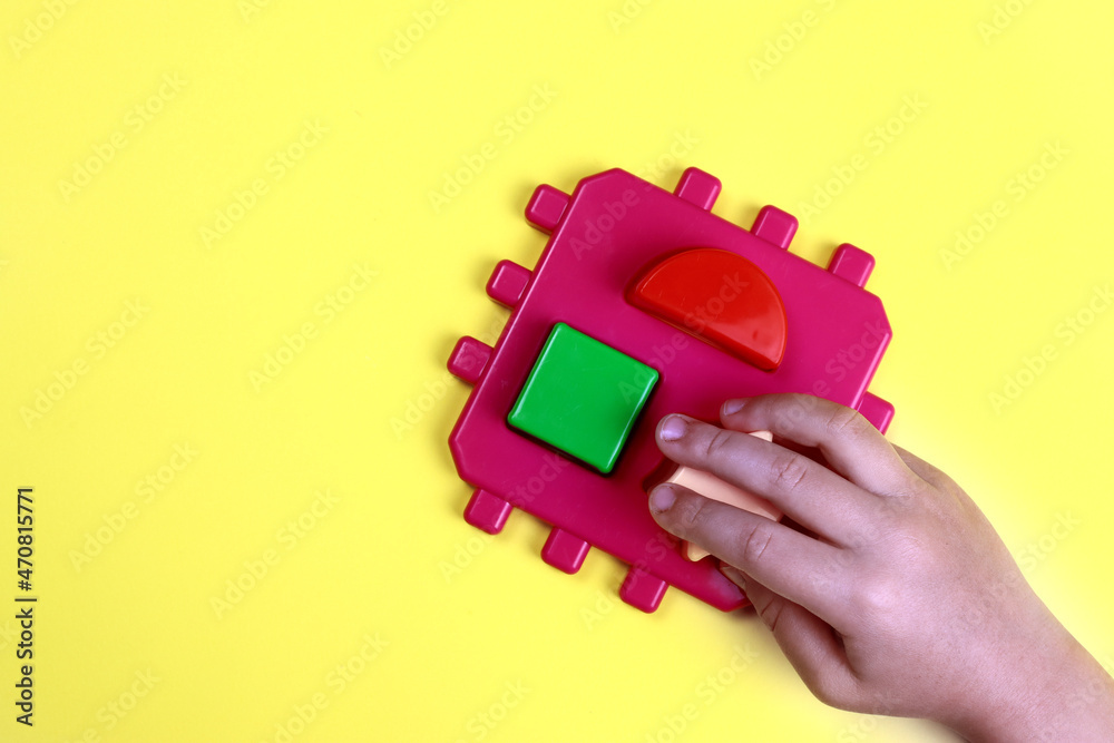 Naklejka premium child plays a developmental constructor on a yellow background, hands close-up