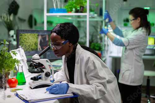 African american biologist scientist analyzing genetic mutation on leaf sample using medical microscope working at biochemistry experiment in microbiology laboratory, Genetically modified plant photo