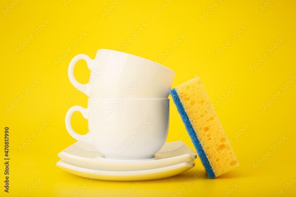 Dishwashing minimal concept. Plates, cups and cleaning sponge against bright yellow background