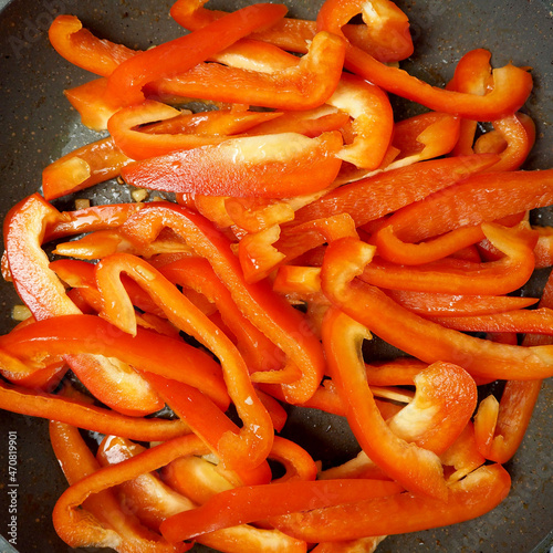 sweet red pepper cut into long pieces lies on a gray frying pan. top view. the cooking process