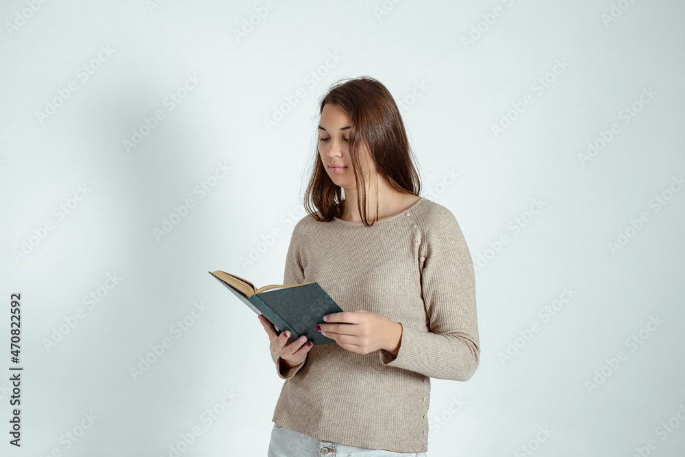 Beautiful female student with a book in her hands on a gray background. The girl is preparing for the exams. Beautiful female student with a book in her hands on a gray background. The girl is preparing for the exams.