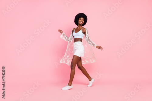 Full size photo of cheerful afro american young woman walk look empty space isolated on pink color background