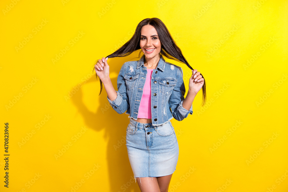 Photo of attractive charming positive young woman hold hands hair wear jeans skirt isolated on yellow color background Photo of attractive charming positive young woman hold hands hair wear jeans skirt isolated on yellow color background
