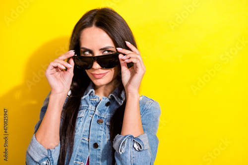 Portrait of attractive cunning girl touching specs looking aside copy space isolated over bright yellow color background