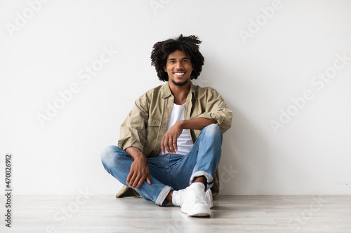 Portrait Of Smiling Handsome Black Guy Relaxing On Floor Near White Wall © Prostock-studio