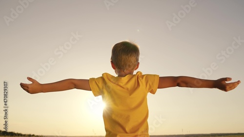 happy child boy prays, spreading his hands to the sides at sunset, kid praying to the sun in sky, pulling helping hand, enjoying freedom outdoors walking in nature in park, inspiring childhood dream