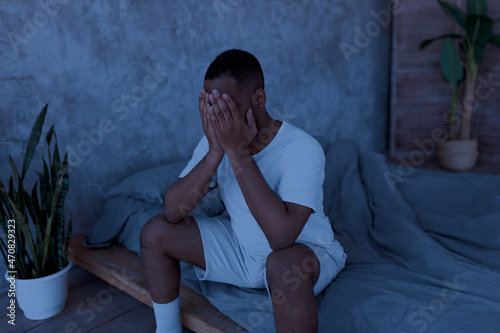 Black man suffering from insomnia sitting on bed