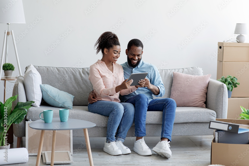 Cheerful smiling young african american husband and wife sitting on sofa, relaxing after moving, buying furniture