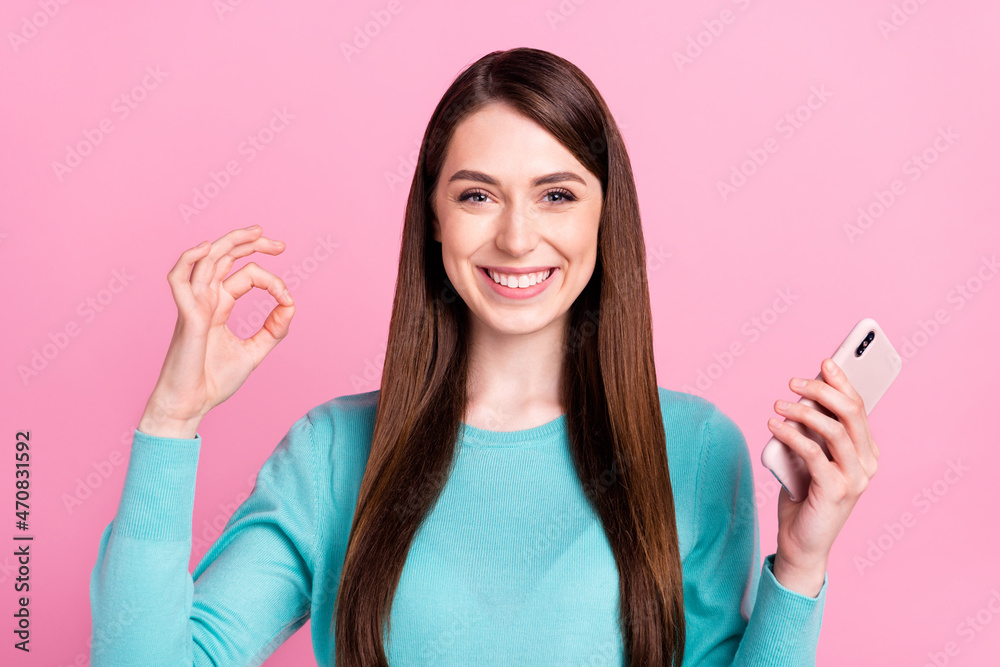 Portrait of attractive cheerful girl holding in hand device showing ok-sign ad isolated over pink pastel color background