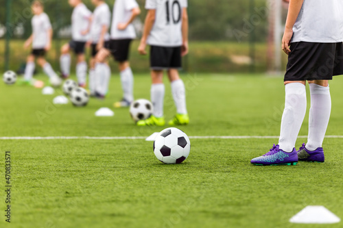 Soccer Players Standing in Line With Soccer Balls on Traininf Unit. Football School For Kids. Young Boys Practicing Soccer on Grass Pitch. Children in White and Black Soccer Kit photo
