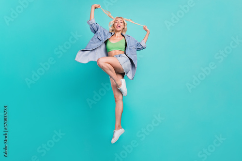 Full body photo of happy positive woman jump up hold hands hair smile isolated on blue color background