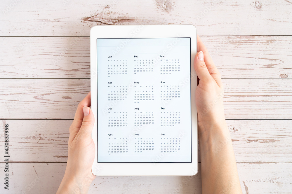 Obraz premium tablet computer with an open app of calendar for unspecified unknown date year without date in a womans hands on a wooden boards background. concept business or to do list goals. top view, flat lay