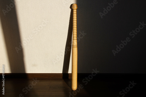A baseball bat stands against the wall. Beautiful shadow of the sun from a Softball Bat falls on the wall. Sport equipment. Carved wooden baseball bat with pattern. Copy space for text. Close-up