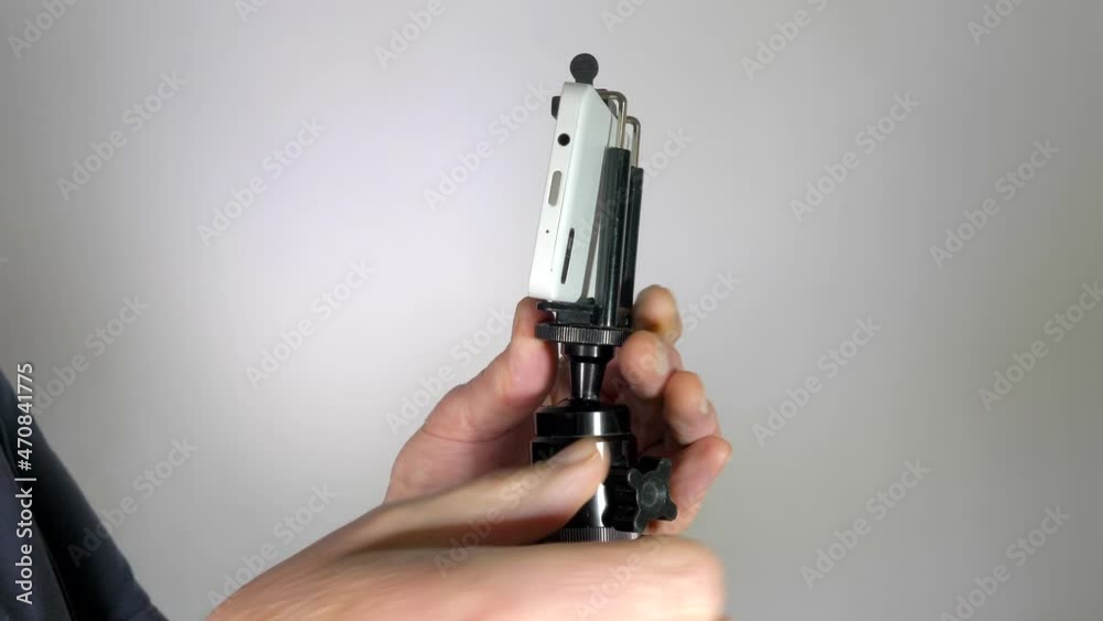 Man’s hands using professional equipment to take a picture with mobile / cell phone, by adjusting a ball head to position the phone in a holder clamp, then touching the screen to take a shot. Man’s hands using professional equipment to take a picture with mobile / cell phone, by adjusting a ball head to position the phone in a holder clamp, then touching the screen to take a shot.