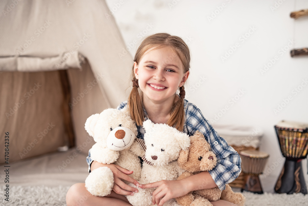 Little girl hugging plush teddies and smiling at camera sitting on floor in playroom Little girl hugging plush teddies and smiling at camera sitting on floor in playroom