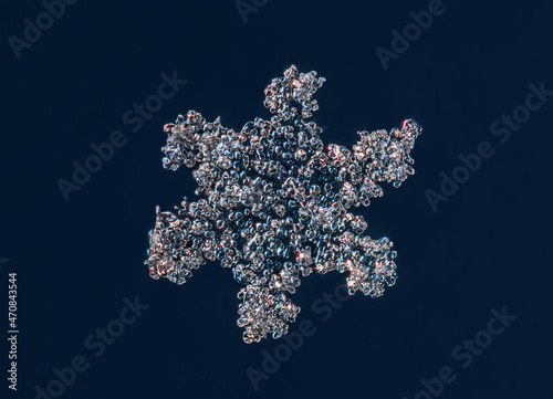 Real snowflake at high magnification. Macro photo of small snow bubbly crystal, snowflake glowing on dark blue background