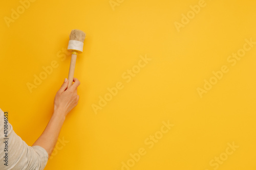 Woman hand holding wooden paint brush on yellow background with copy space. Renovation and improvement equipment. Working tool for house design project and improvement