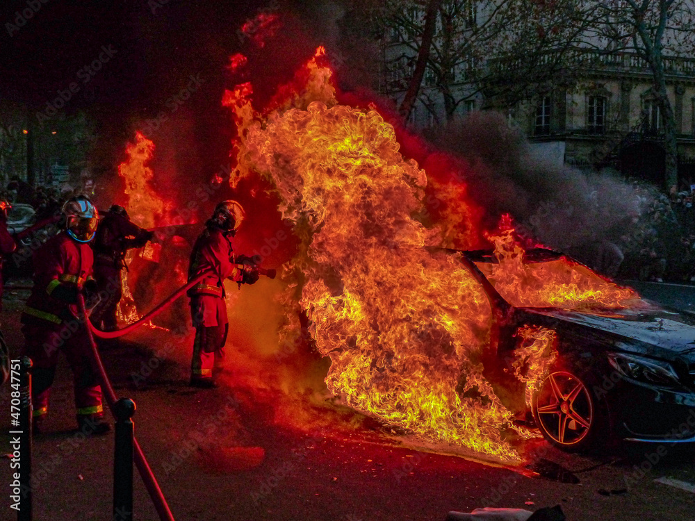 photo prise lors d'une manifestation à Paris. une voiture enflammée que des pompiers tentent d'éteindre