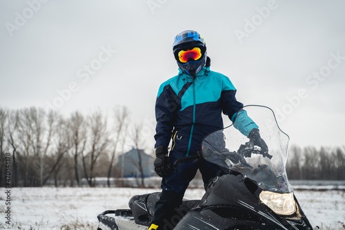 Snowmobile driver stands on his black snowmobile in a snowy area, cross helmet photo
