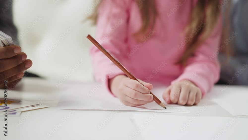 Little girl student writes letters with pencil on paper sheet learning English language with African-American teacher at home lesson closeup slow motion Little girl student writes letters with pencil on paper sheet learning English language with African-American teacher at home lesson closeup slow motion