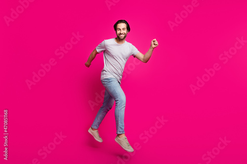 Photo of cheerful handsome guy jump run move wear striped t-shirt jeans footwear isolated pink color background