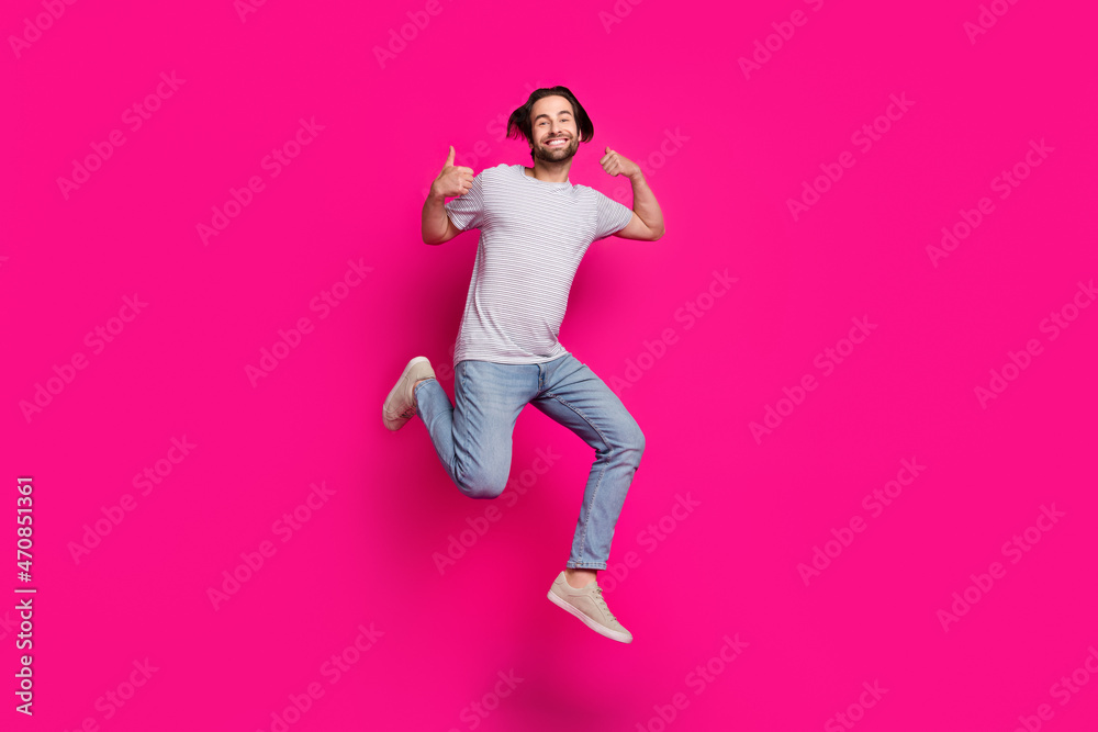 Photo of confident reliable guy jump raise two thumbs up wear striped t-shirt jeans sneakers isolated pink color background