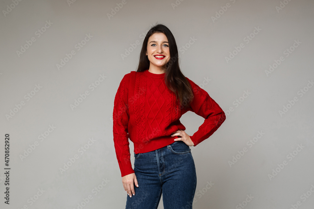 Happy smiling young brunette girl in red warm sweater posing on gray background Happy smiling young brunette girl in red warm sweater posing on gray background