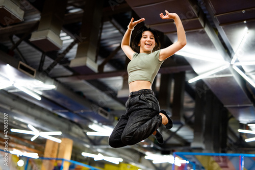 Pretty girl jumping on colorful trampoline at playground park and smiling. Female teenager during active entertaiments indoor photo