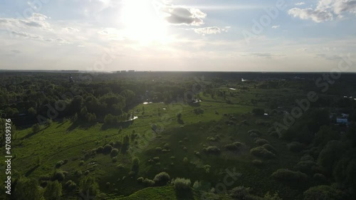 Russia, Moscow region, Pushkino city, Klyazma district. Aerial video of a flight over a summer green field before sunset. Video shows nature - the Klyazma River, young trees and a church at distance. photo
