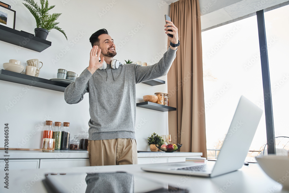 Man waving and attentively looking at the smartphone screen while having video call Man waving and attentively looking at the smartphone screen while having video call