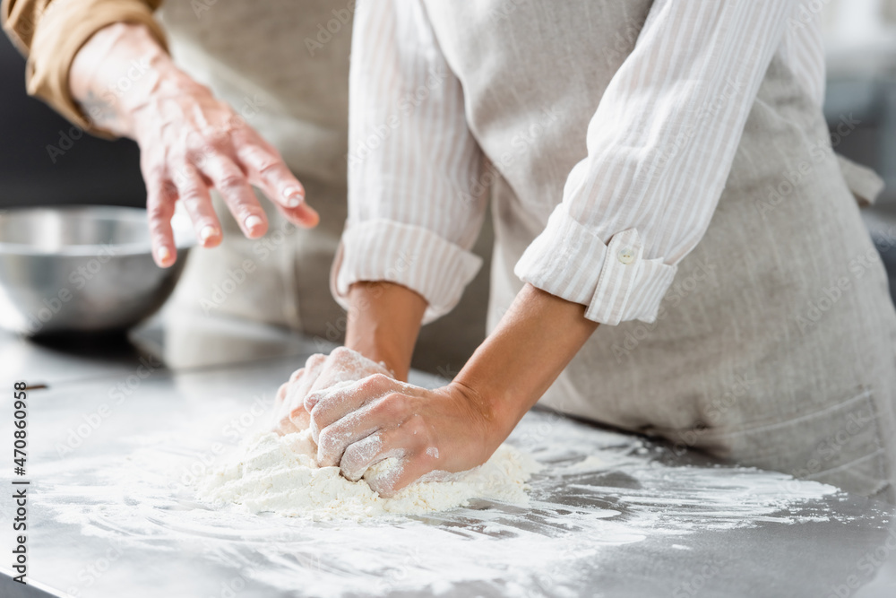 Cropped view of chef making dough near colleague pointing with hand in kitchen