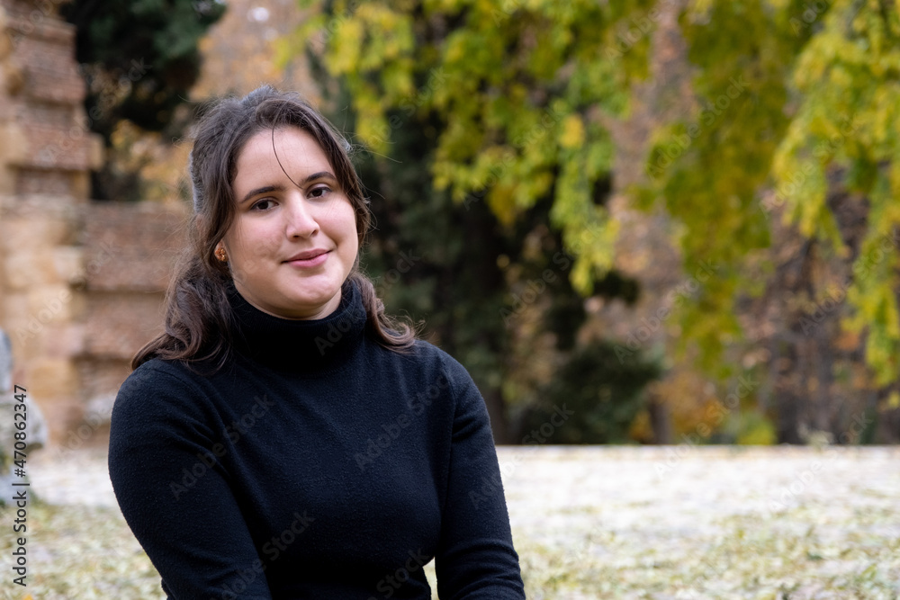 Happy girl smiling looking directly at camera .Portrait of a young European Caucasian woman wearing a black sweater outdoors on a park in autumn Happy girl smiling looking directly at camera .Portrait of a young European Caucasian woman wearing a black sweater outdoors on a park in autumn