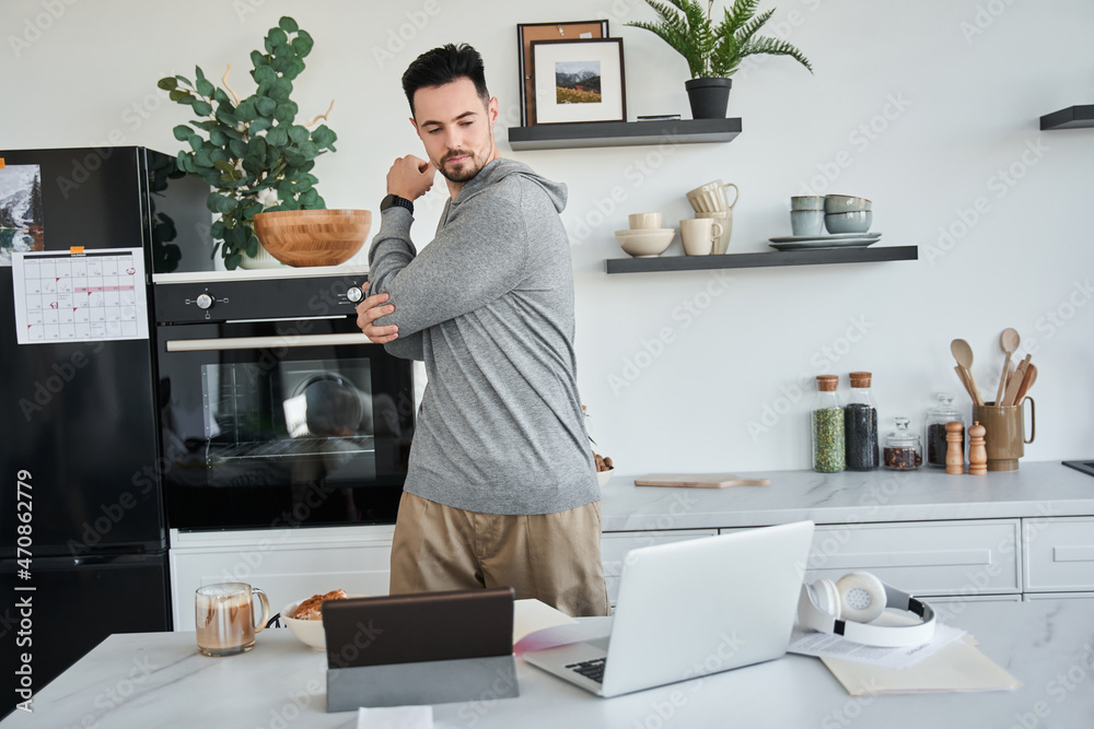 Man looking at the laptop screen while standing and stretching arms at the kitchen Man looking at the laptop screen while standing and stretching arms at the kitchen