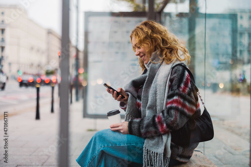 Fotografia, Obraz Young woman using smart phone at bus station