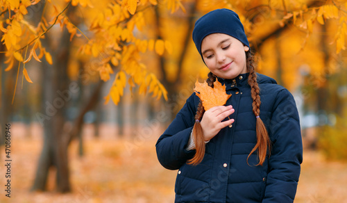 Portrait of a child girl in autumn city park. Posing with maple leaf. Beautiful nature  trees with yellow leaves.