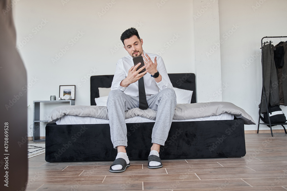Businessman sitting at the bed and chatting via online call at his smartphone