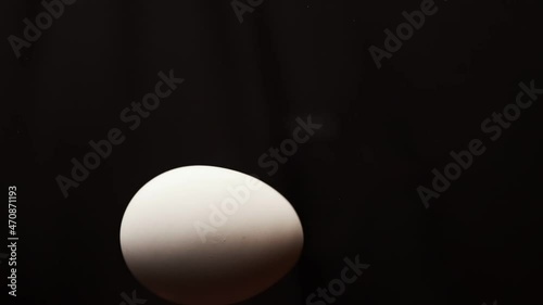Egg is spinning on a black background. Slow motion of an egg in a shell spinning on glass. Close shot of a spinning egg.