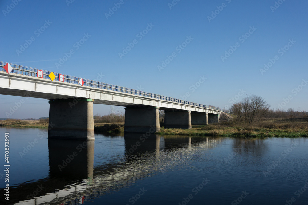 Road bridge with blue sky in the background. View from side. Straight road line with empty copy space. Old rusty road barriers texture. Bridge over river landscape.