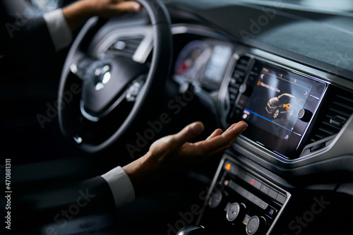 Close up of male person in stylish suit examining multimedia system of luxury car while choosing new vehicle at showroom. Concept of people, transport and selling. 
