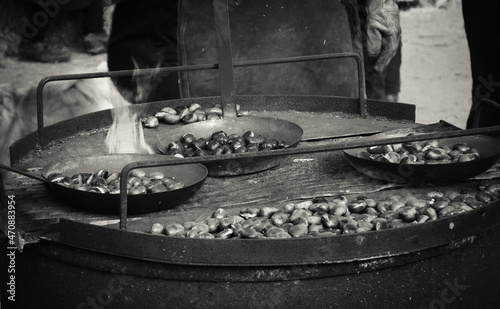 Chestnuts roasted in old iron pans over the fire at traditional Christmas medieval fair in Provins, France. Comfort food background. Black white historic photo .