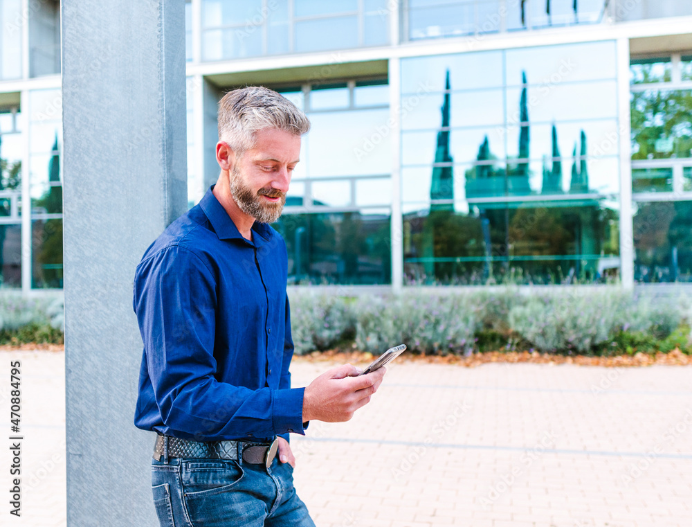 Bearded man leaning on pillar and scrolling smartphone Bearded man leaning on pillar and scrolling smartphone