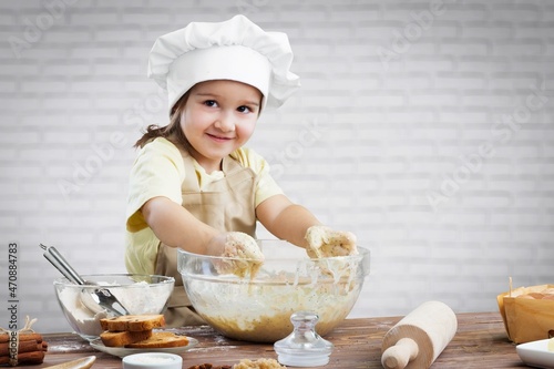 Toddler child playing with the dough in the kitchen dressed as a chef. Child baking a cake