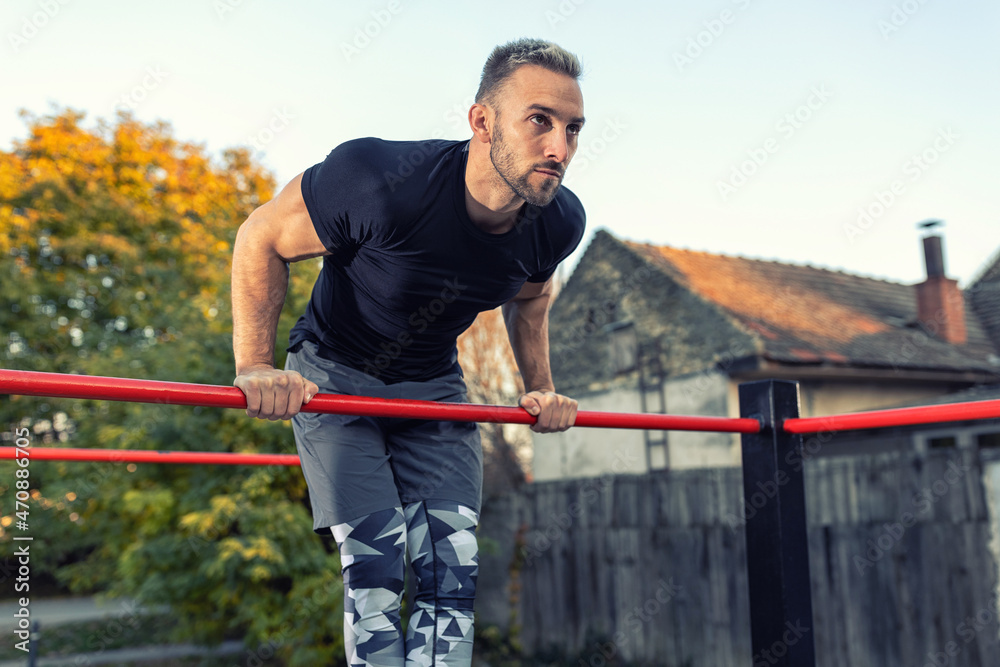 Young muscular man doing calisthenics outside lifting himself above the bar, street gymnastics