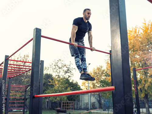 Фотография Young muscular man doing calisthenics outside lifting himself above the bar, str