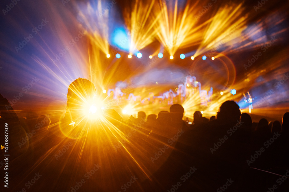silhouette of the audience at a music concert. the happy audience dances and applauds their idols. bright multicolored spotlights illuminate the stage and the auditorium