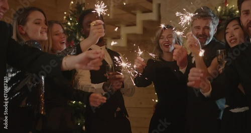  Group of Friends, wearinf in fashinable clothes, holding Sparkles during Celebration of New Year in decorated restaurant photo